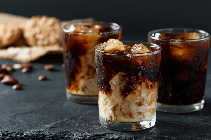 Three iced coffee drinks with cream swirls in short glasses on a dark slate surface