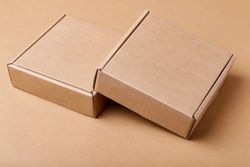 Two plain kraft cardboard mailer boxes stacked at a slight angle on a brown surface
