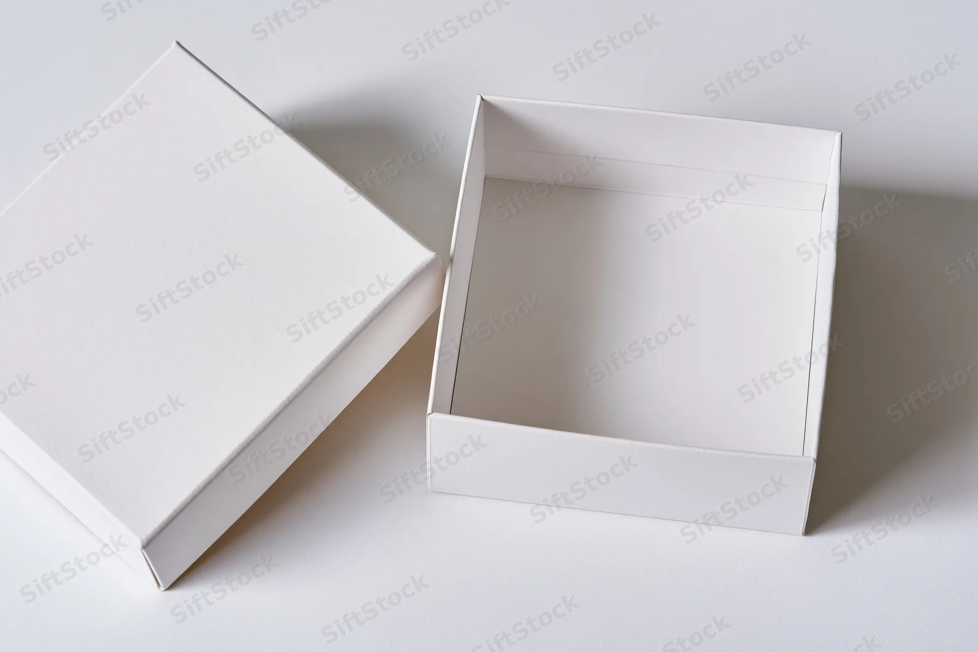 Two plain white cardboard gift boxes, one open and one closed, arranged on a white surface