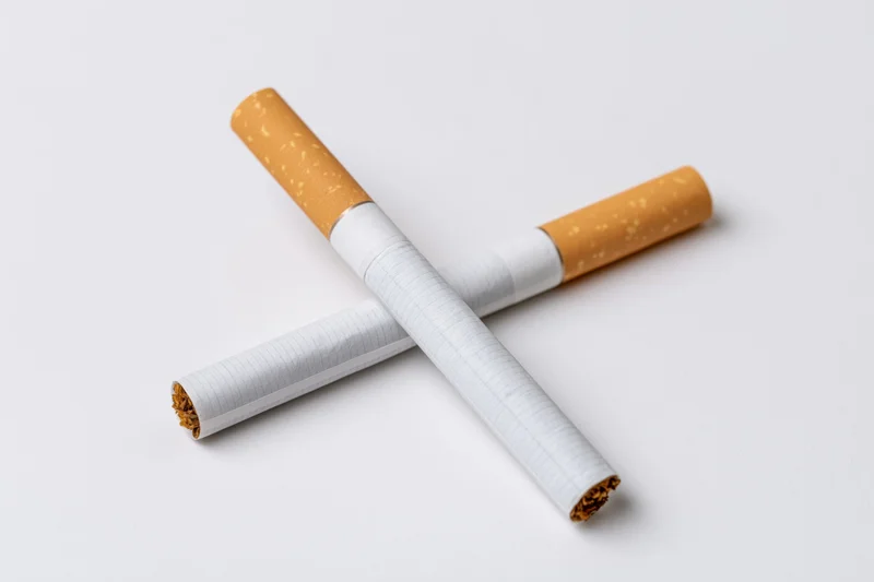 Two unlit cigarettes crossed on a plain white surface