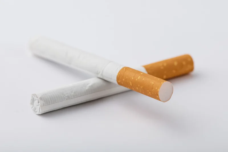 Two unlit cigarettes crossed on a plain white surface