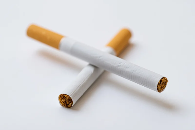 Two unlit cigarettes crossed on a plain white surface