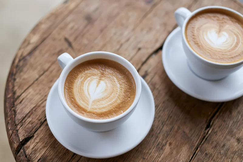 Two white ceramic cappuccino cups with tulip latte art on a rustic wooden table
