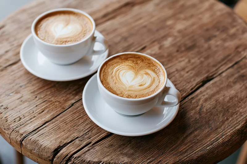Two white ceramic cappuccino cups with heart-shaped latte art on a rustic wooden table