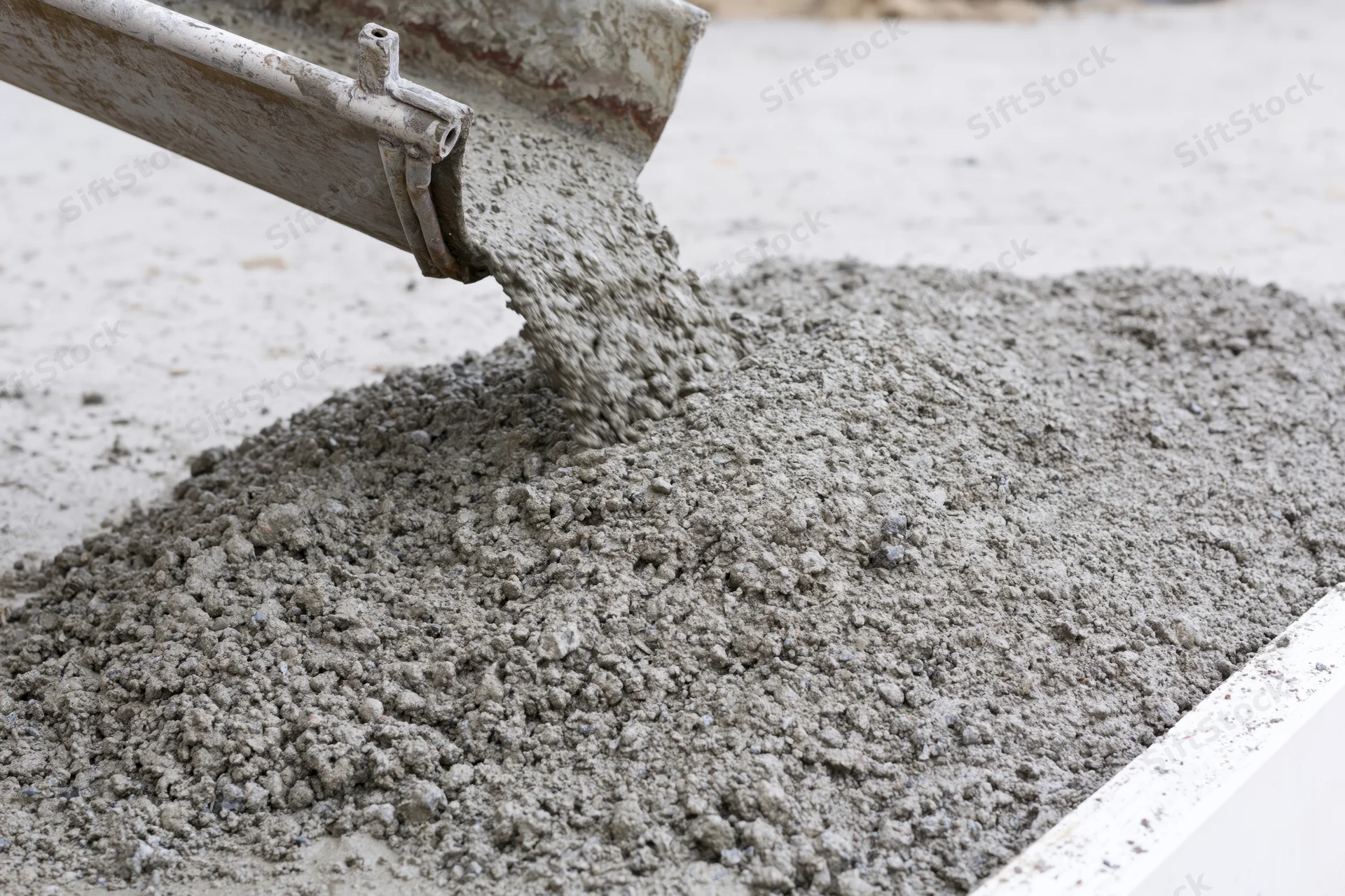 Wet concrete pouring from a metal chute onto a flat construction surface
