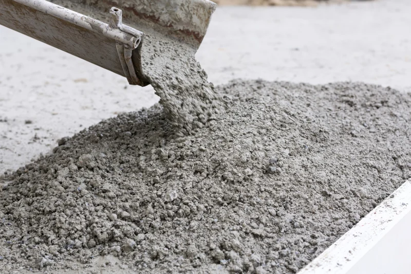 Wet concrete pouring from a metal chute onto a flat construction surface