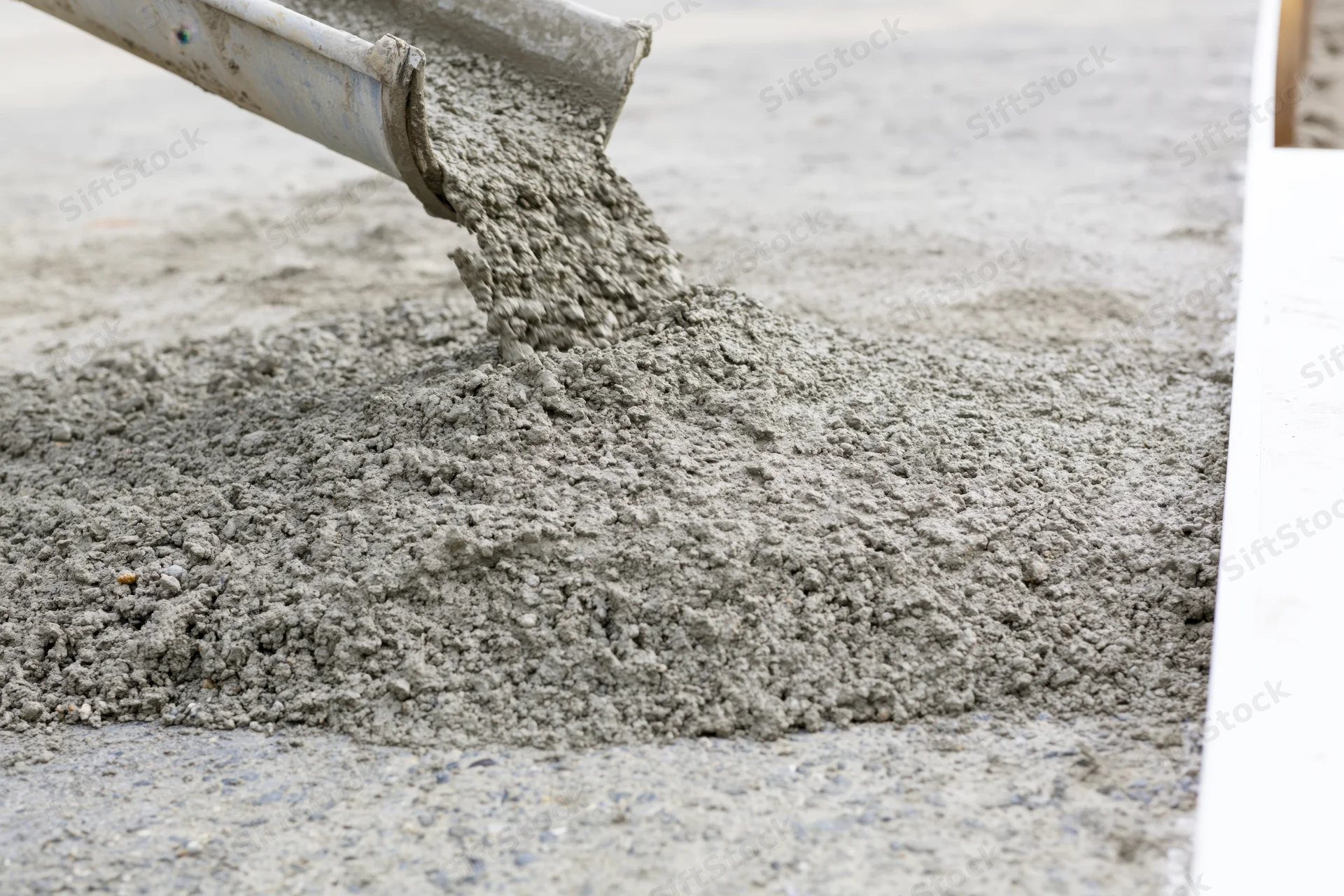 Wet concrete pouring from a metal chute onto a flat construction surface