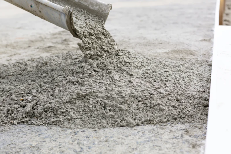Wet concrete pouring from a metal chute onto a flat construction surface