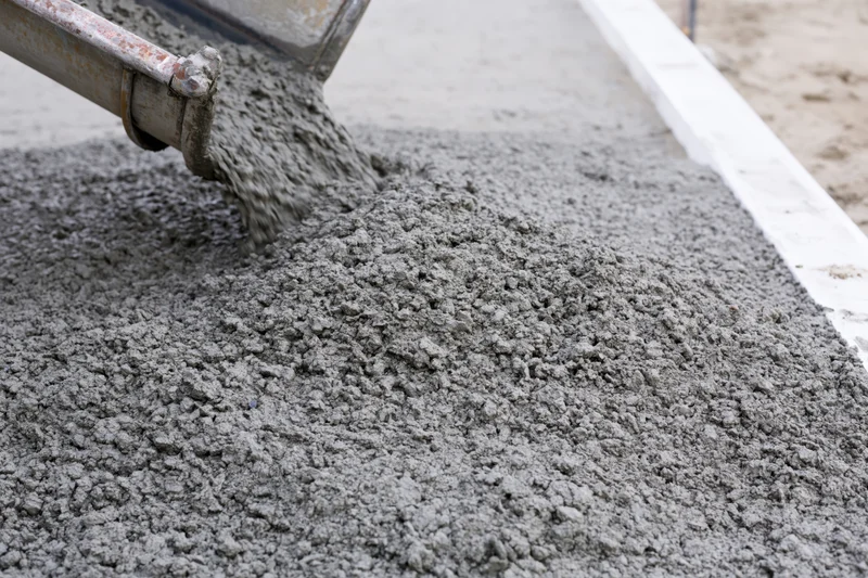 Wet concrete pouring from a metal chute onto a flat construction surface