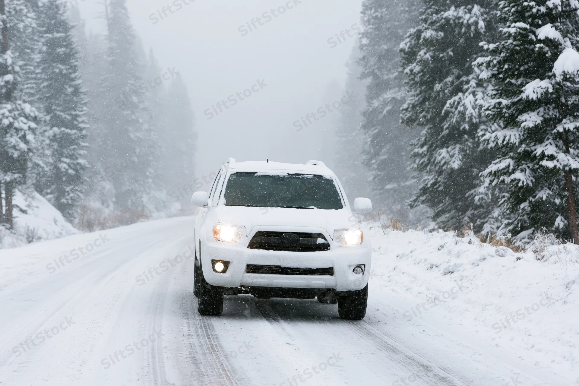 White suv driving on snow-covered mountain road surrounded by snow-laden evergreen trees during snowfall