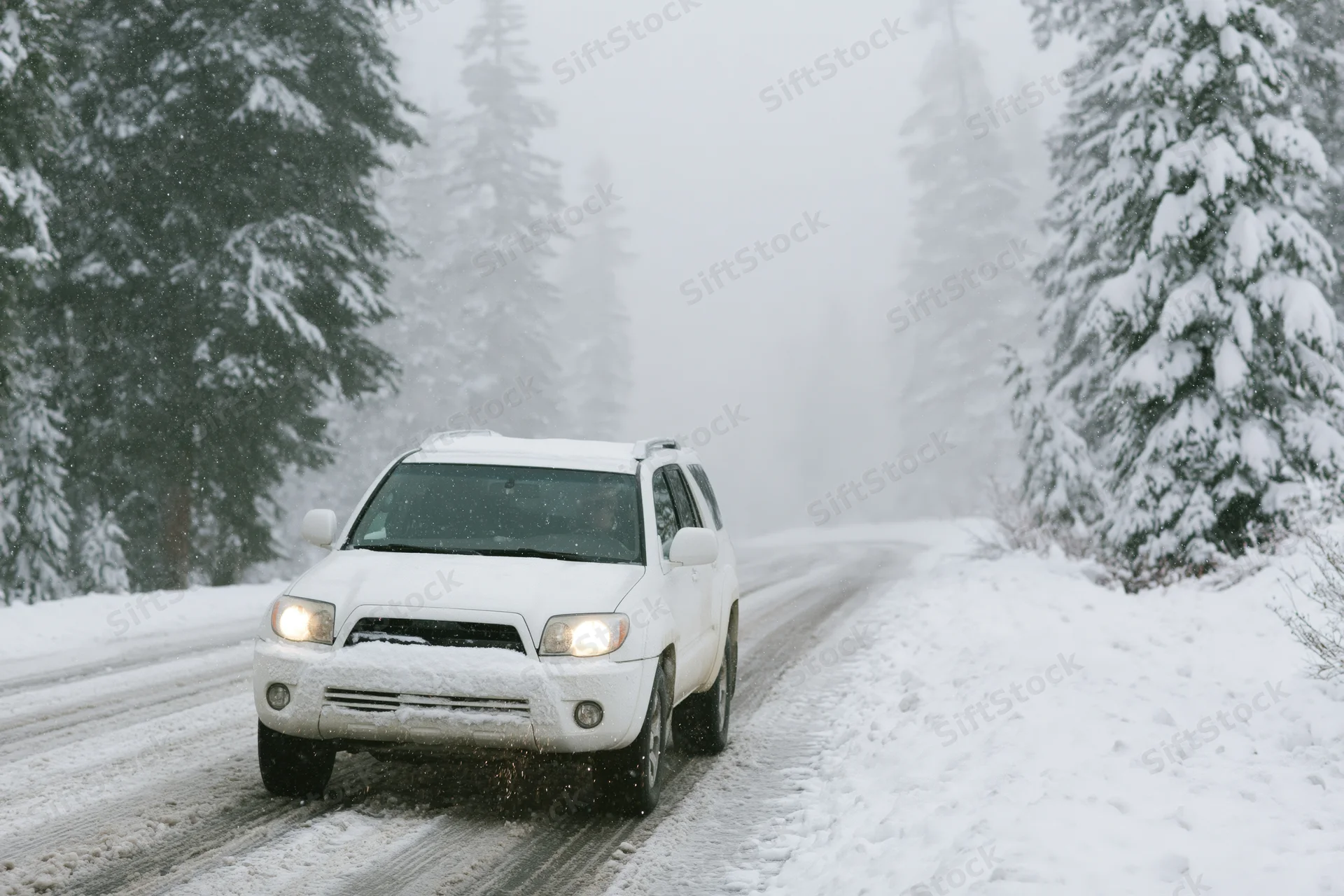 White suv driving on snow-covered mountain road surrounded by snow-laden pine trees during winter storm