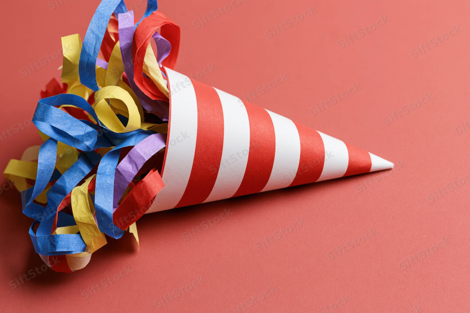 Red and white striped party popper cone lying on its side with colorful streamers spilling out on a solid red background