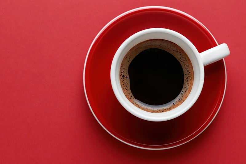 White ceramic coffee cup filled with black espresso on red saucer viewed from above