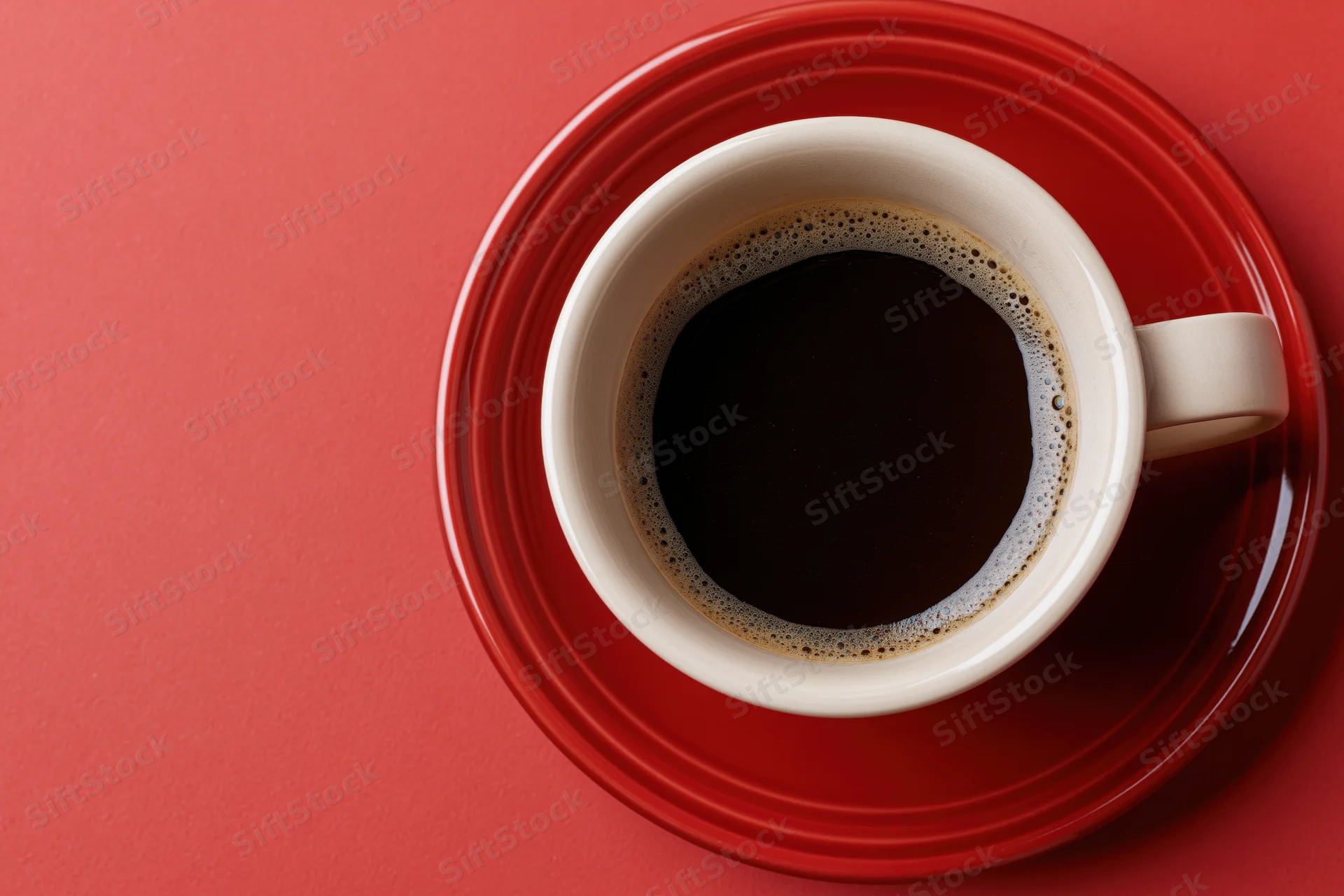 White ceramic coffee cup filled with black espresso on red saucer viewed from above