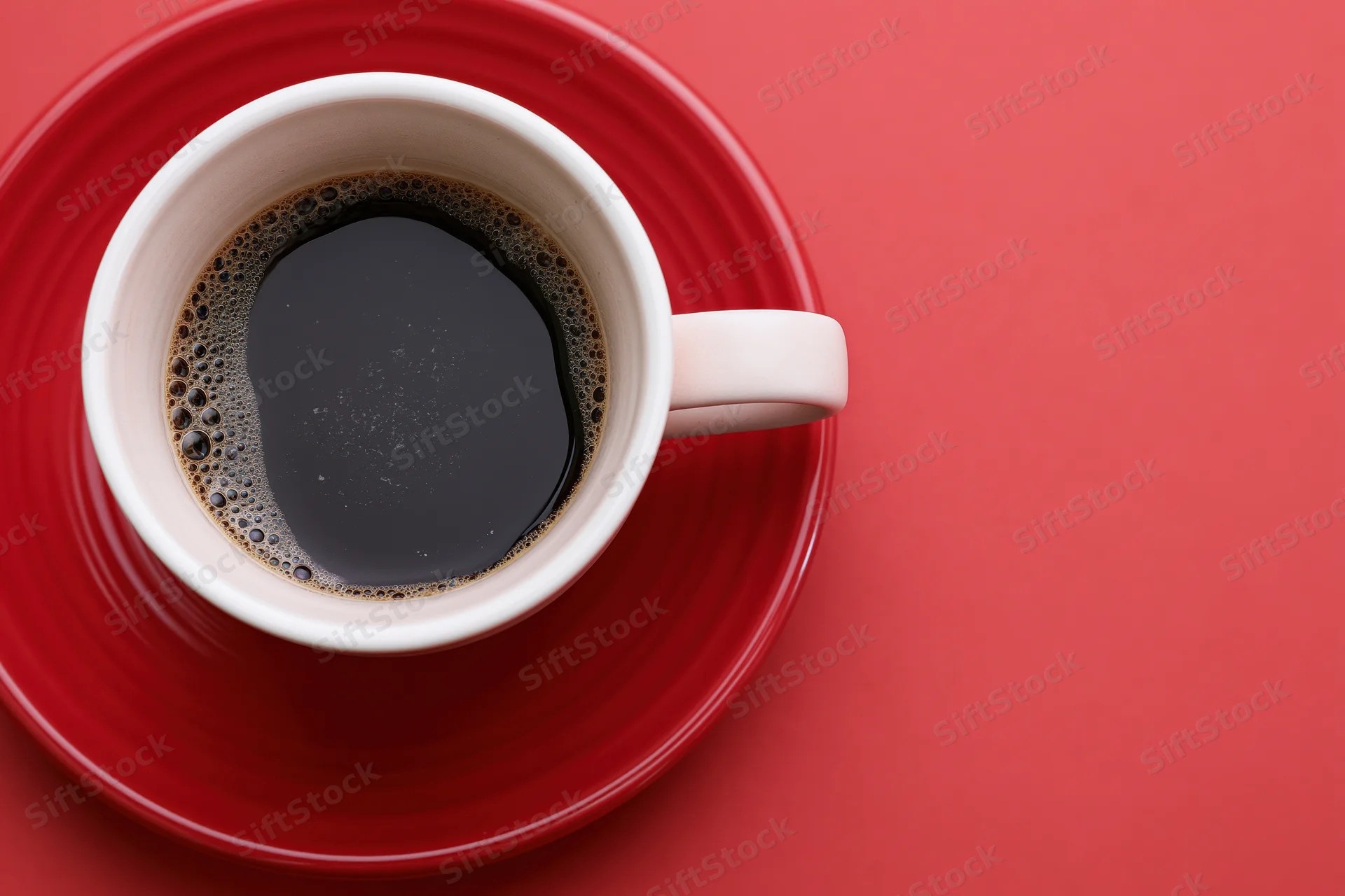 White ceramic coffee cup filled with black espresso on red saucer against red background