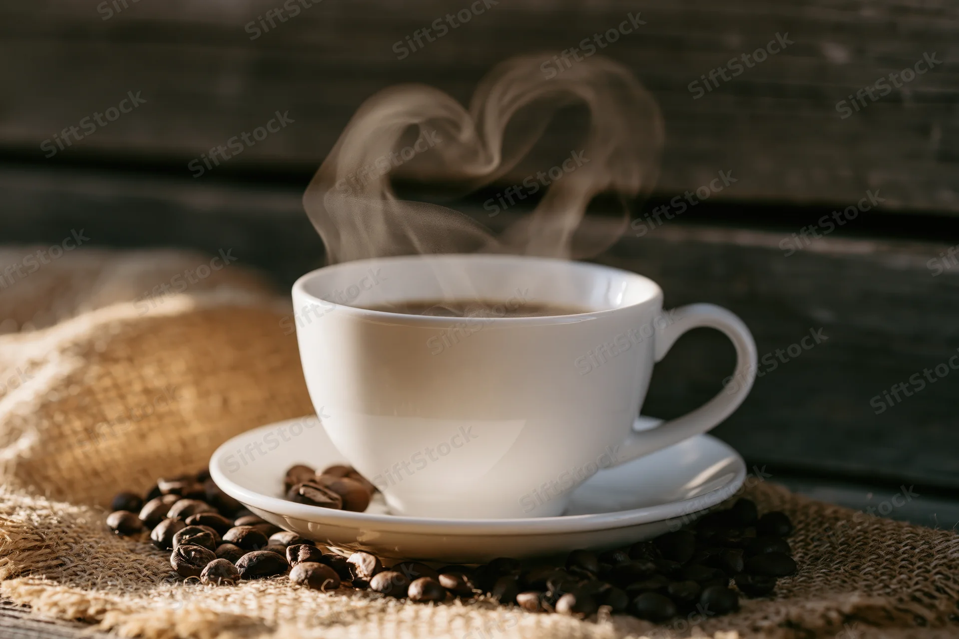 White ceramic coffee cup on saucer with steam rising, surrounded by coffee beans on burlap over wooden surface
