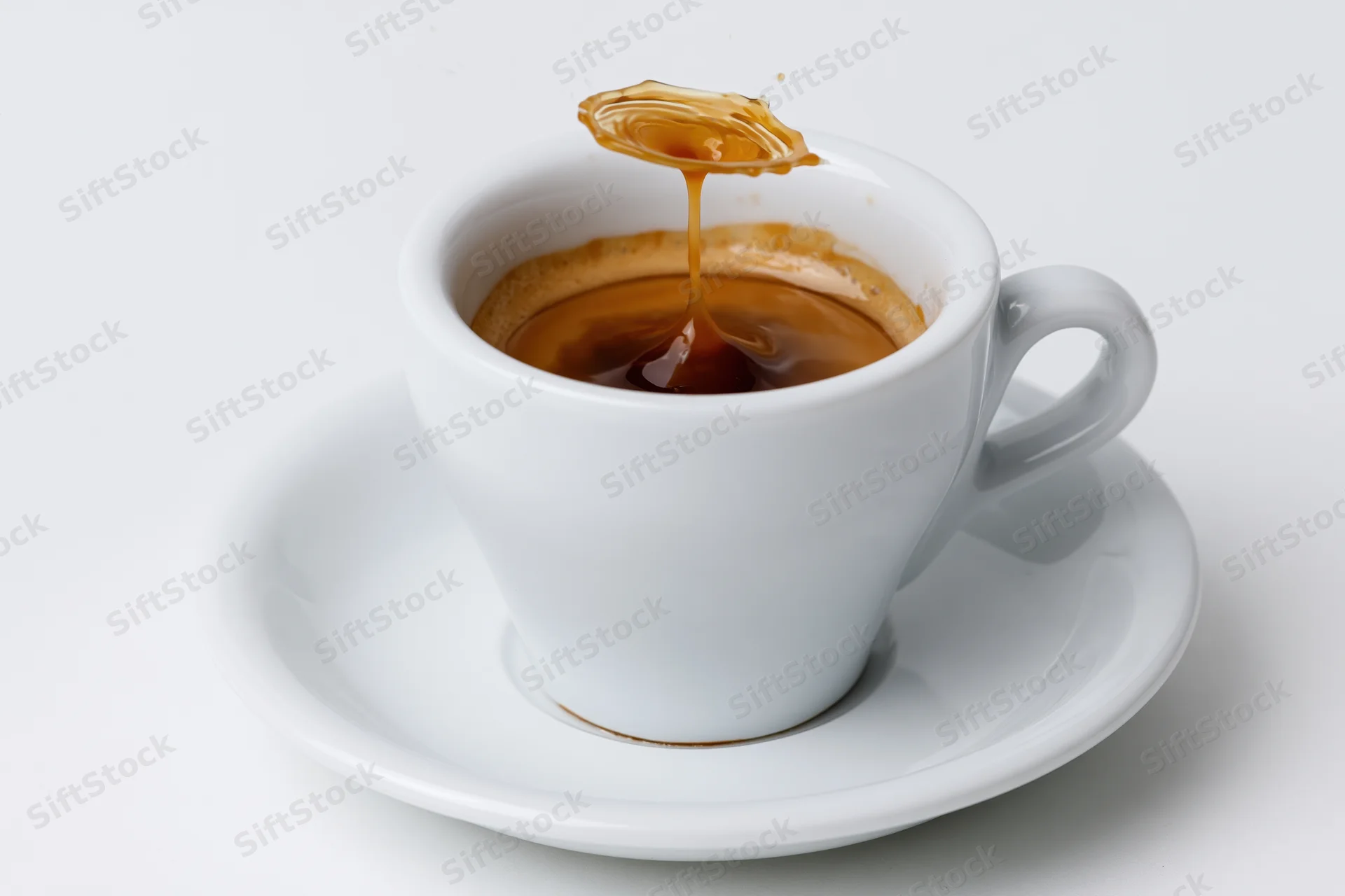 White ceramic espresso cup with caramel syrup dripping into the coffee on a matching saucer
