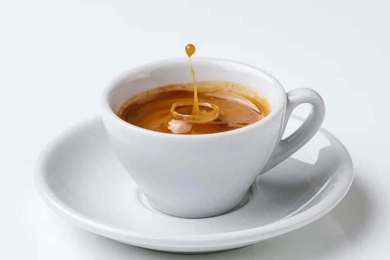 White ceramic espresso cup with a single drop falling into the coffee creating a splash ring on the saucer
