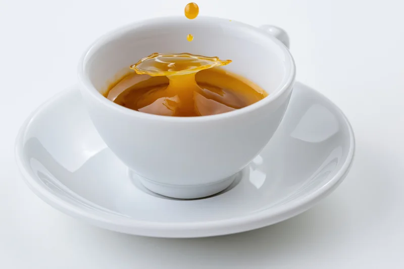 White ceramic espresso cup with a single drop falling into the coffee creating a splash on a matching saucer