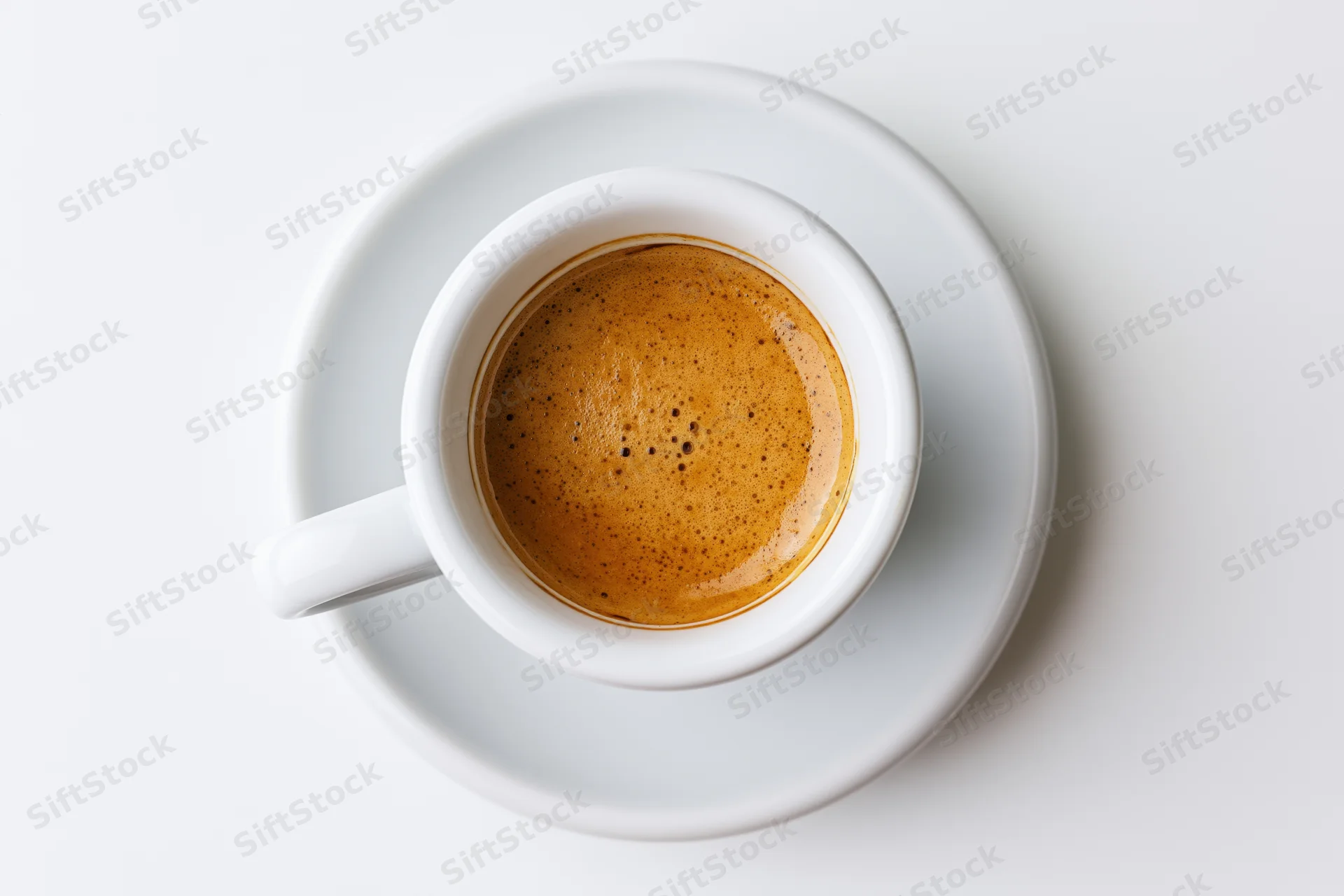 White ceramic espresso cup filled with coffee and crema on matching saucer, top-down view on plain white surface