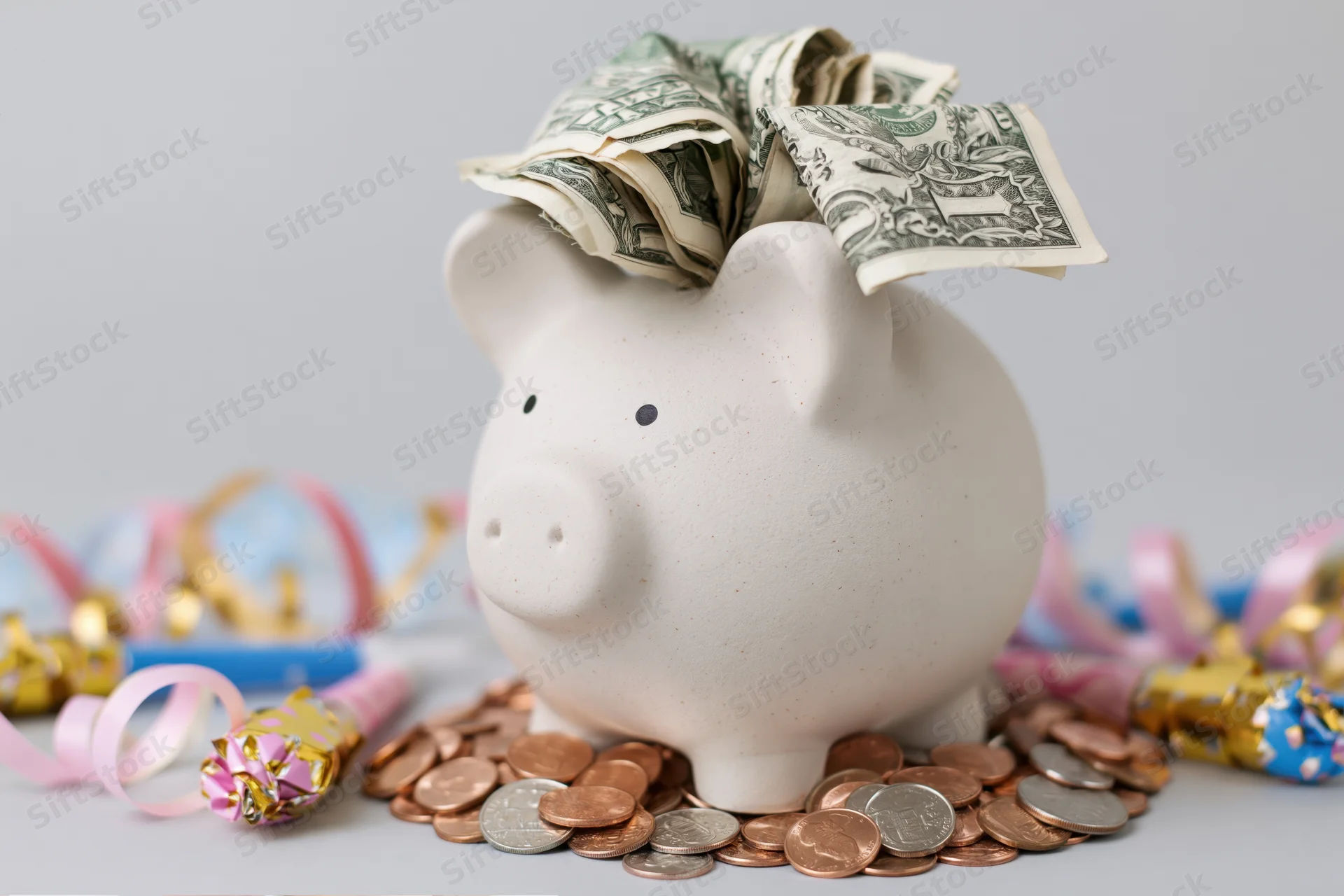White ceramic piggy bank stuffed with folded us dollar bills surrounded by coins and festive decorations on a plain surface