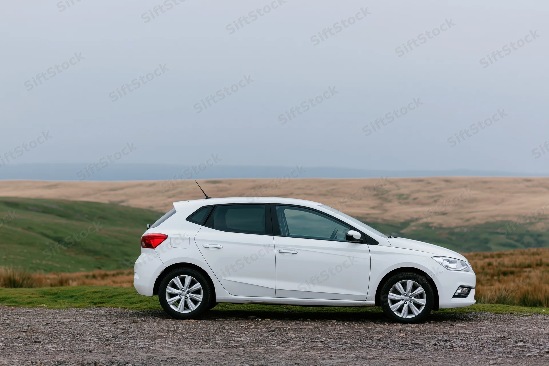 White compact hatchback parked on gravel roadside pullout in rural landscape