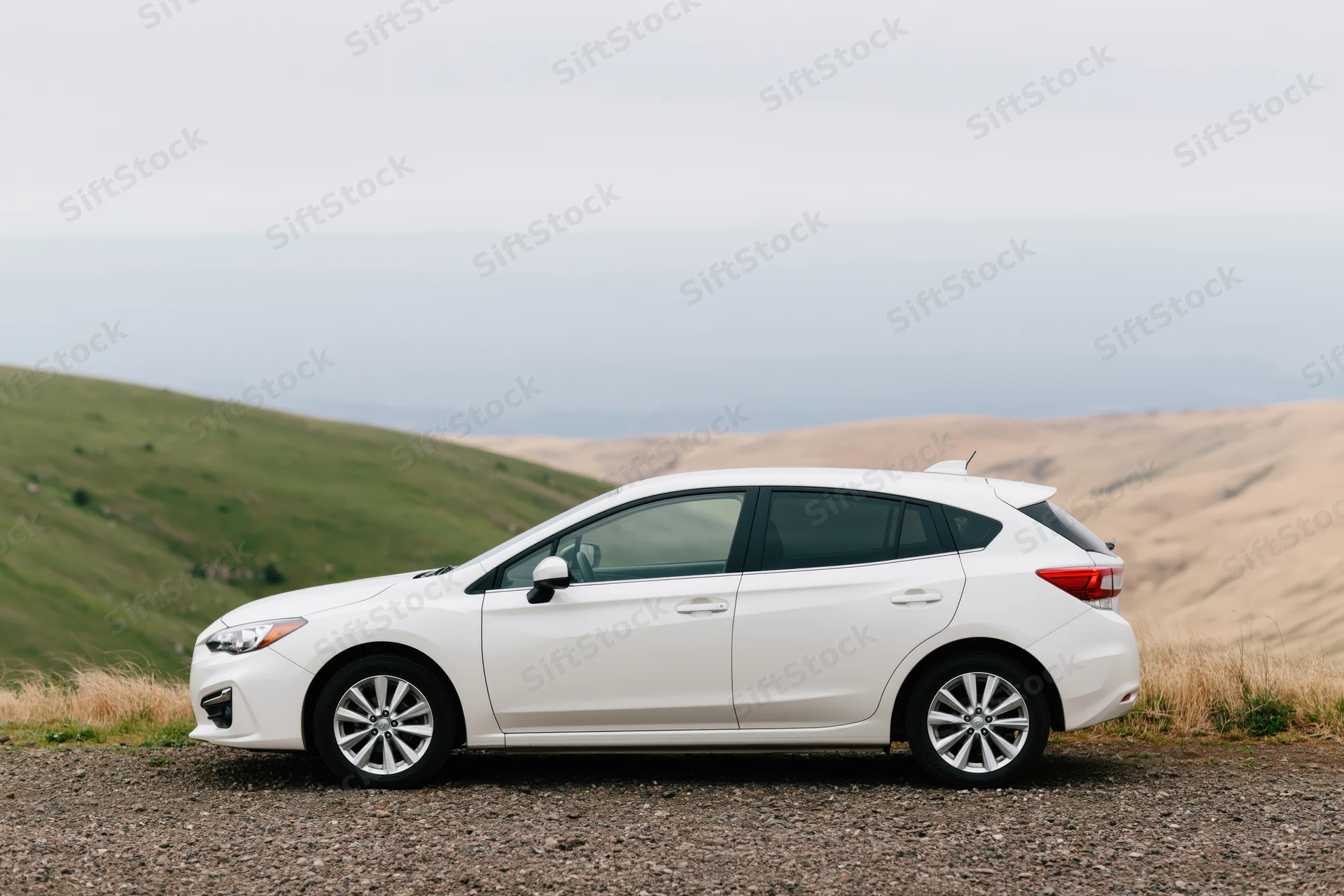 White compact hatchback parked on gravel roadside pullout with rolling hills in background