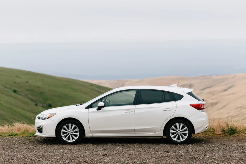 White compact hatchback parked on gravel roadside pullout with rolling hills in background