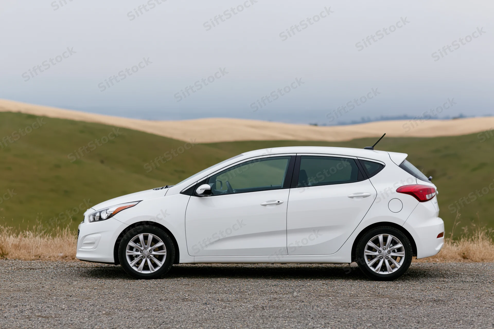White compact hatchback parked on gravel roadside pullout with rolling hills in background