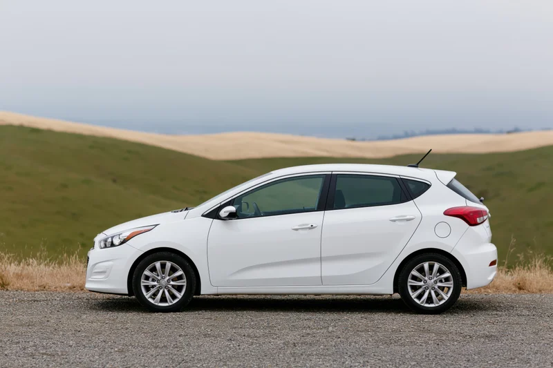 White compact hatchback parked on gravel roadside pullout with rolling hills in background