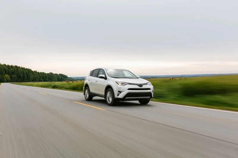 White midsize suv driving on rural two-lane asphalt road past green fields and trees