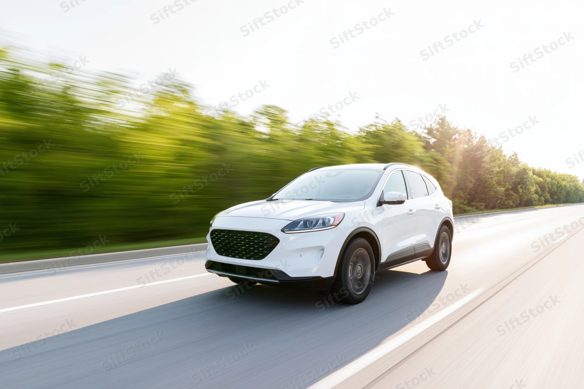 White mid-size suv driving at speed on a two-lane road with blurred green trees alongside