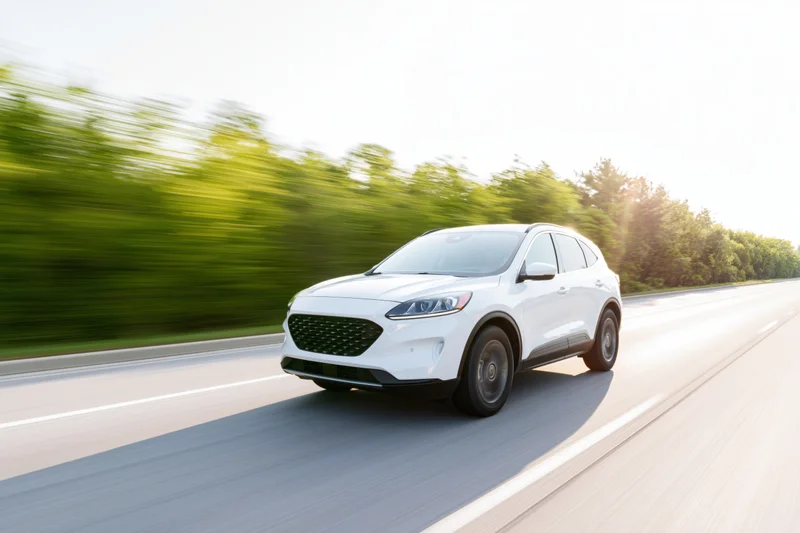 White mid-size suv driving at speed on a two-lane road with blurred green trees alongside