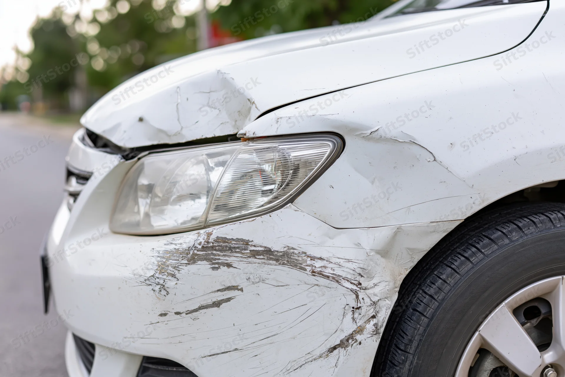 White sedan with dented and scraped front fender and headlight on asphalt road