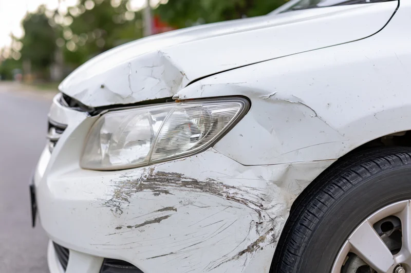 White sedan with dented and scraped front fender and headlight on asphalt road