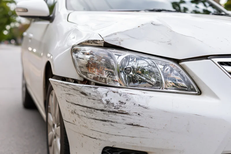 White sedan with dented and scraped front passenger fender parked on pavement
