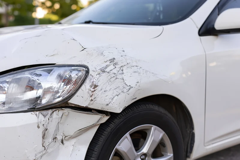 White sedan with dented and scraped front passenger fender outdoors