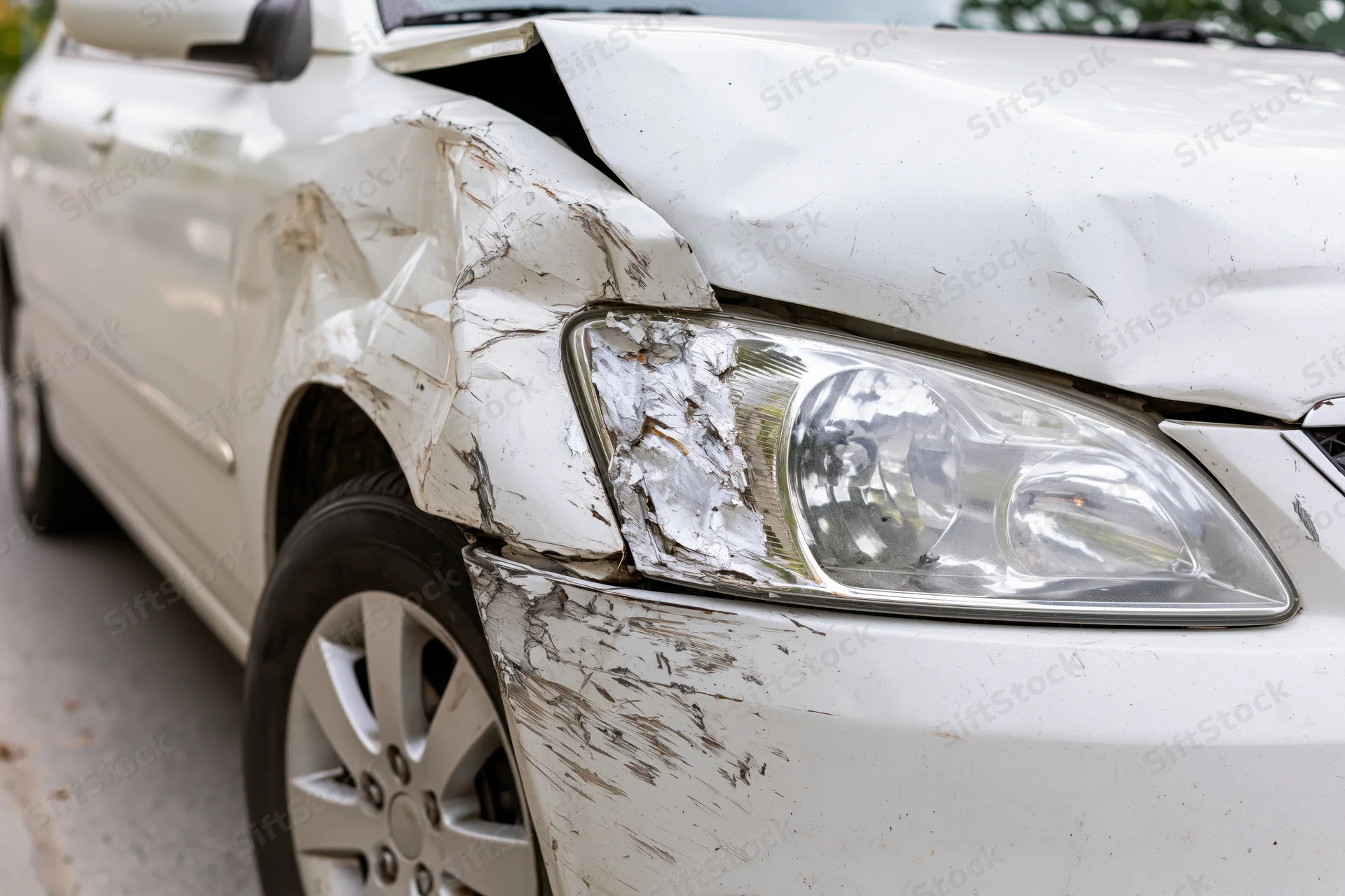 White sedan with dented and scraped front passenger fender and headlight damage