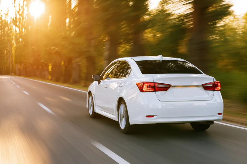 White sedan driving away on a two-lane country road at sunset