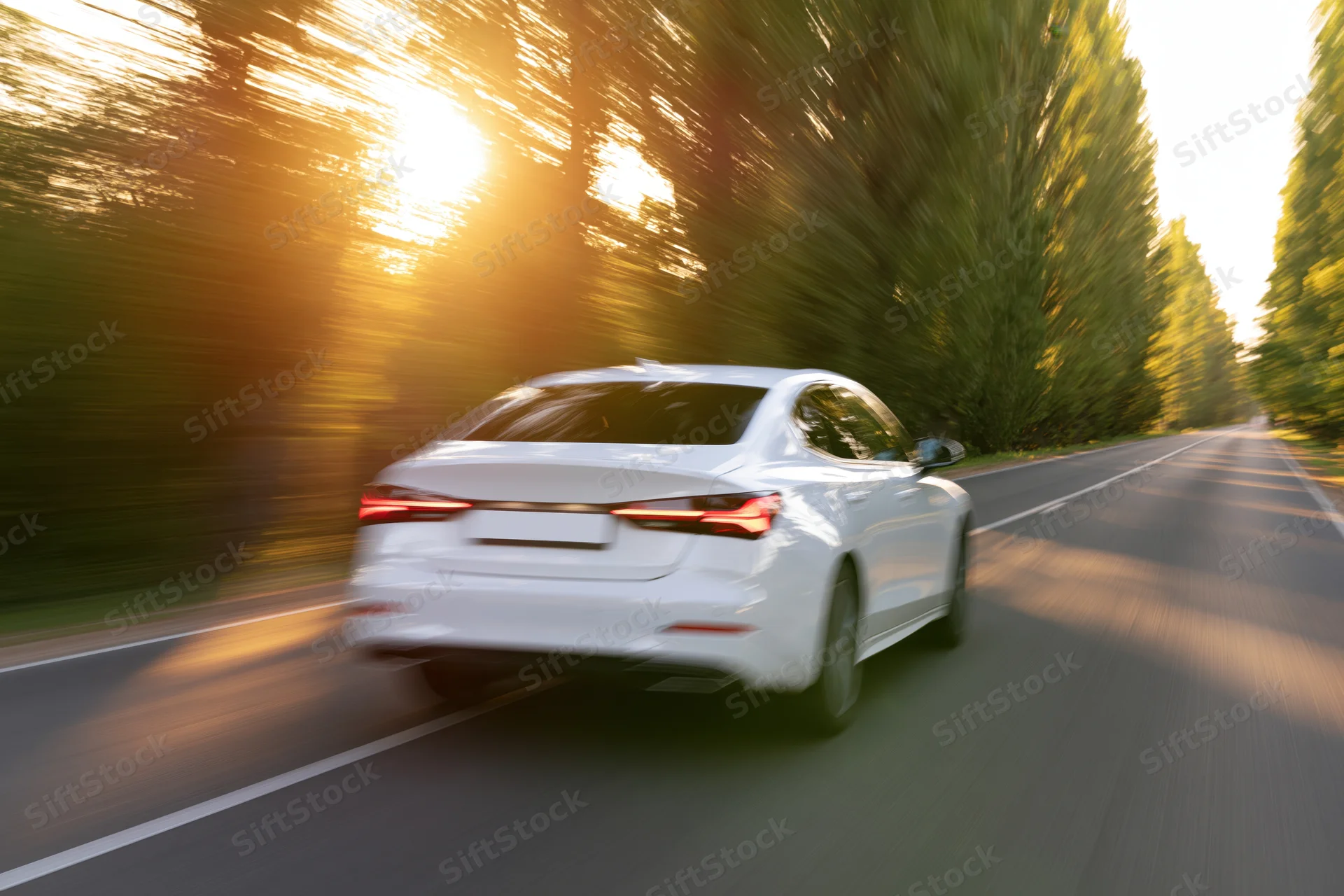 White sedan driving away on a two-lane country road at sunset