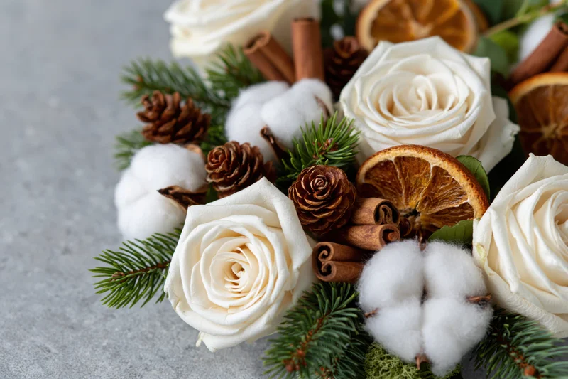 Winter floral arrangement with white roses, pine, cotton, cinnamon and dried orange on grey stone surface