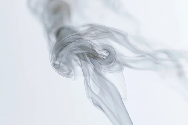 Wispy smoke curling and dispersing in mid-air against a pure white background