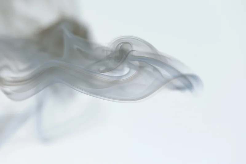 Wispy smoke curling and dispersing mid-air against a pure white background