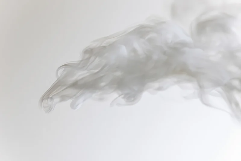 Wispy white smoke drifting and dispersing against a plain background
