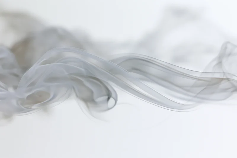 Wispy smoke tendrils drifting and curling across a pure white background