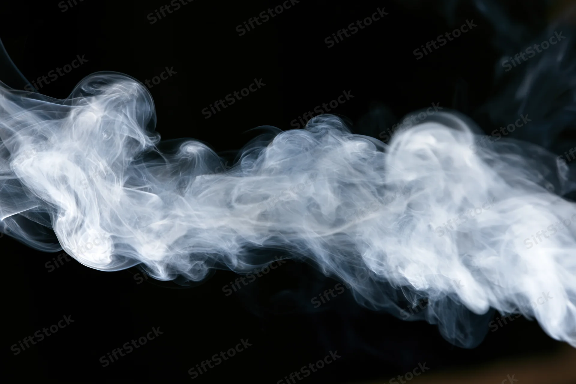 Wispy white smoke tendrils curling and dispersing mid-air against black background