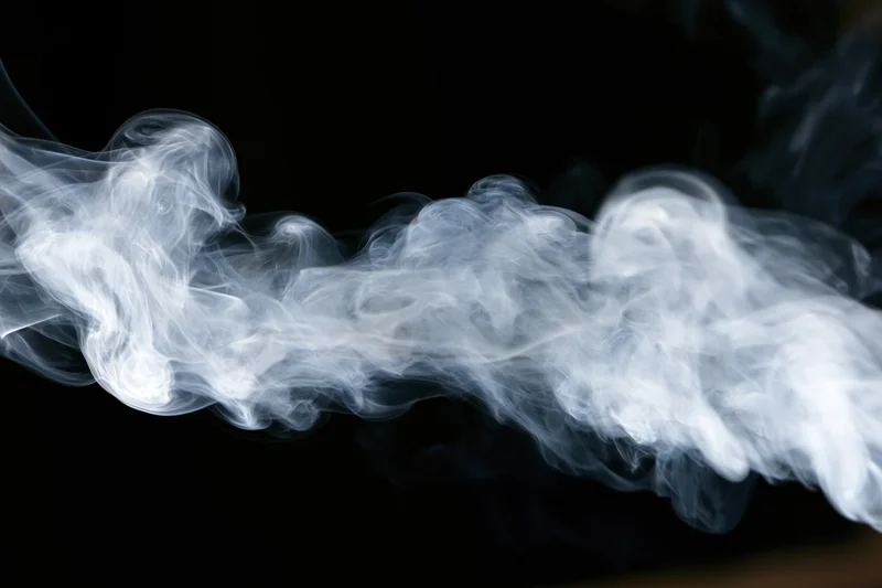 Wispy white smoke tendrils curling and dispersing mid-air against black background