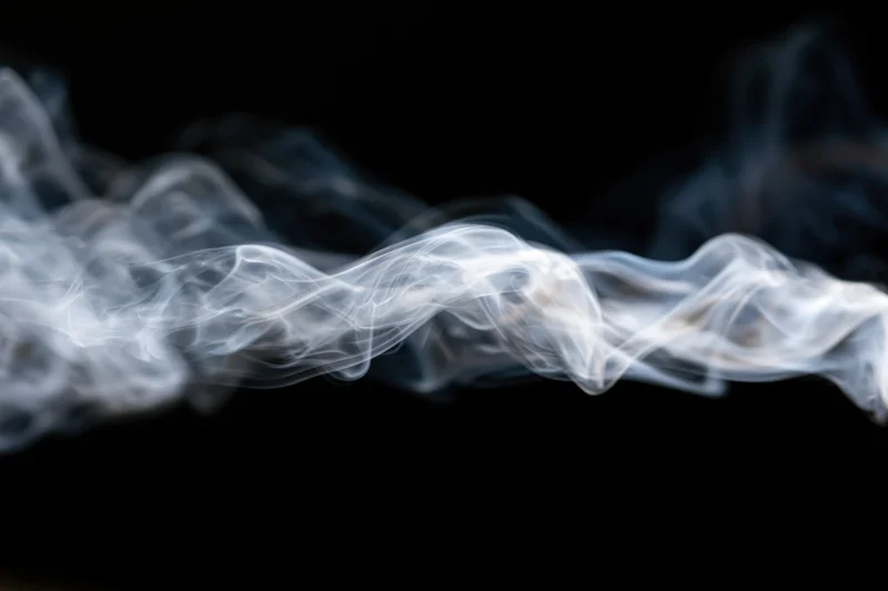 Wispy white smoke tendrils curling and dispersing mid-air against black background