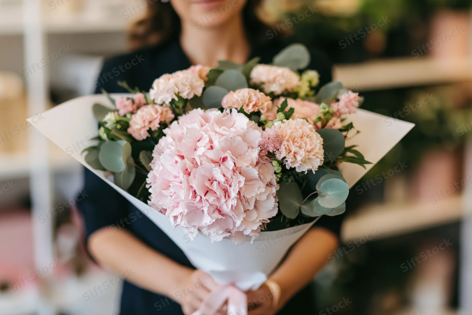 Woman holding a large bouquet of blush pink hyacinths and peonies wrapped in white paper with eucalyptus leaves