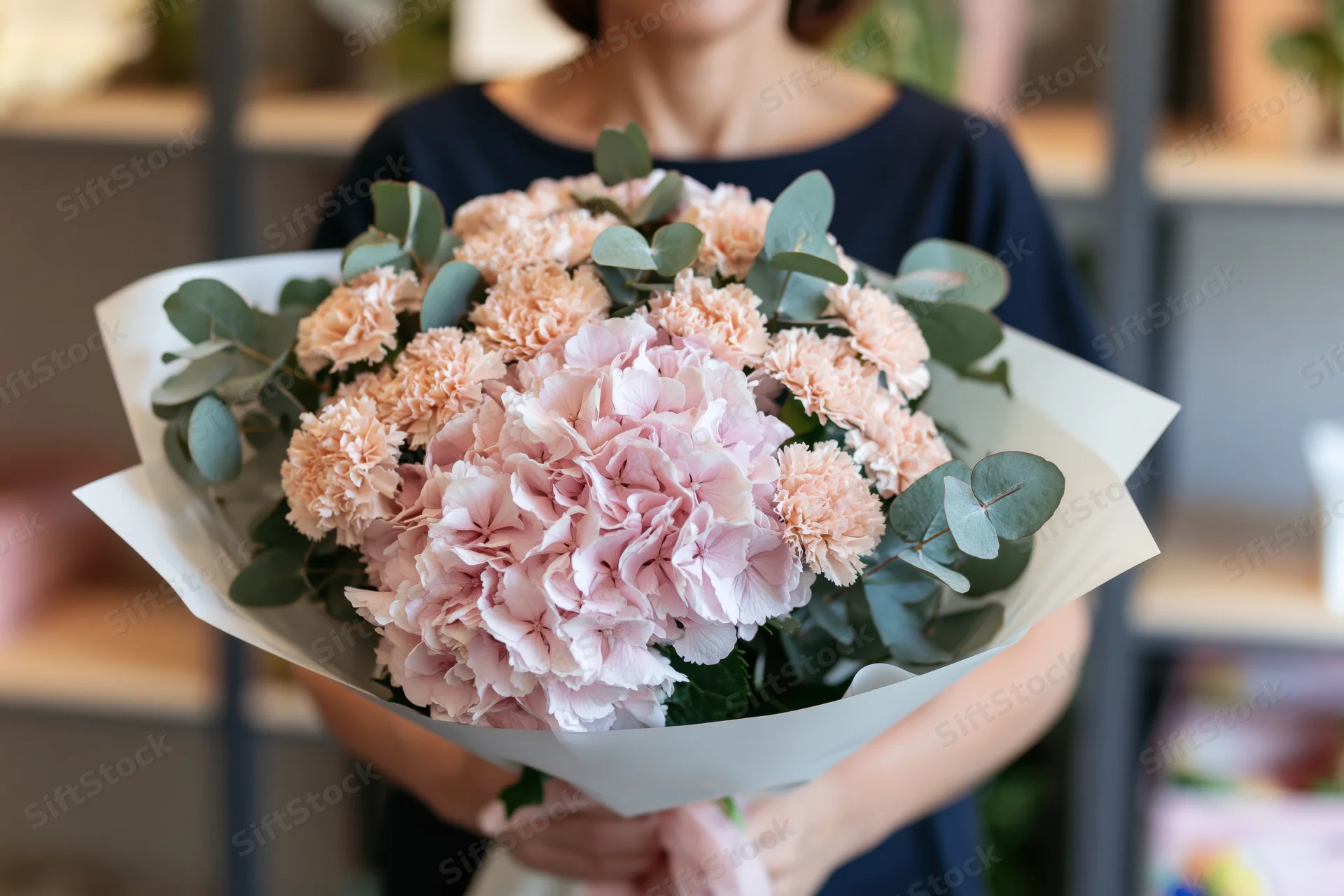Woman holding a large bouquet of blush pink hydrangeas and carnations with eucalyptus foliage wrapped in paper